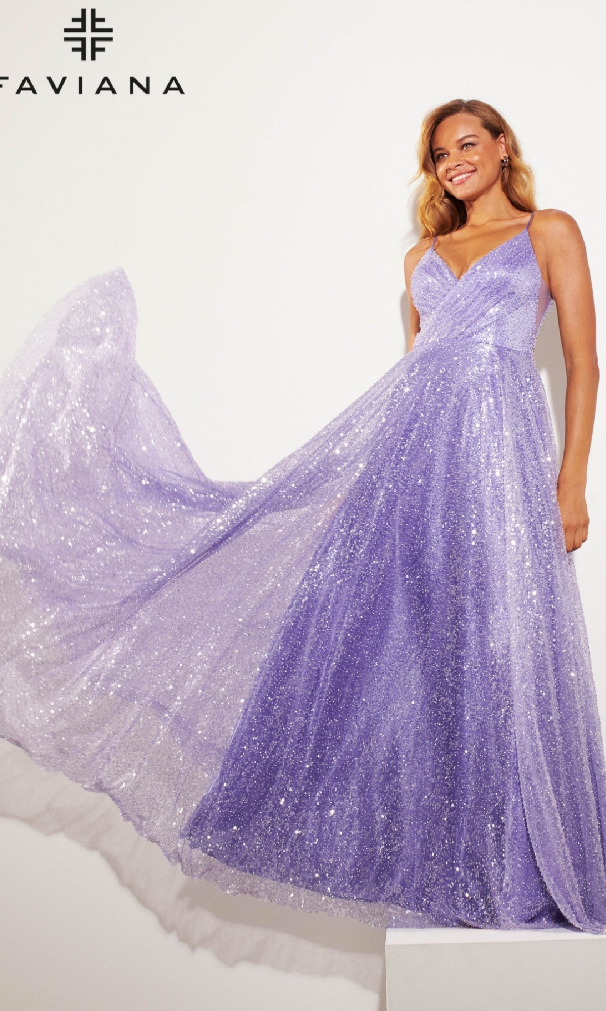 A woman poses against a white background in the Faviana 11203 Long Sequin A-Line Prom Dress, holding up one side of the sparkling lavender gown. The